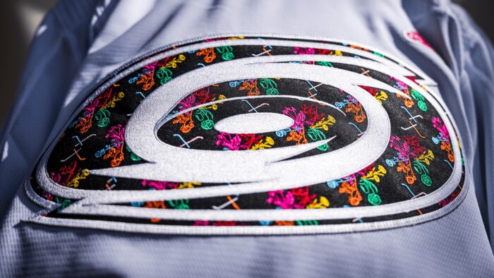 Macro of the Carolina Hurricanes Pride jersey crest: the hurricane warning flag logo filled with embroidered violets, roses and carnations