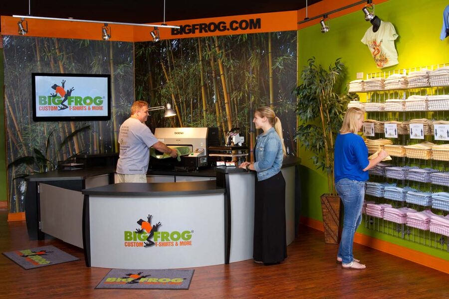 Inside a Big Frog store, staff at a direct-to-garment printer behind the counter