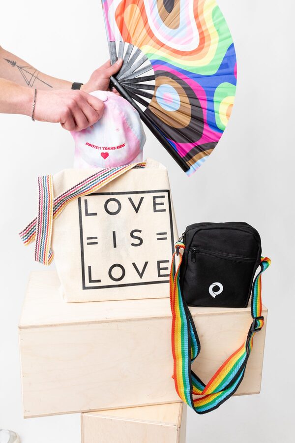 Queerencia products including a Protect Trans Kids cap and a Love Is Love tote